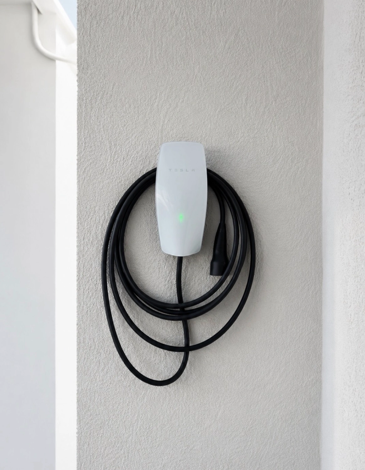 White wall-mounted EV charger with a coiled charging cable