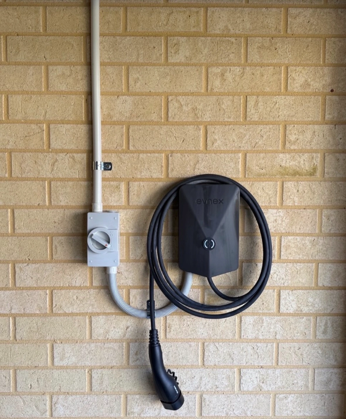 Black EV charger and charging cable installed on an exterior brick wall